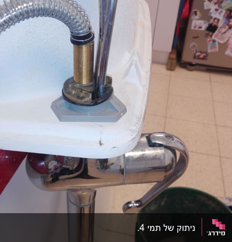 כיור עם ברז וצינורות מתכת, דלי ירוק על הרצפה